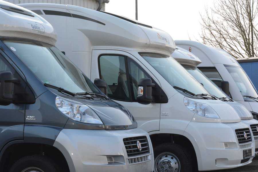 En række hvide autocampere parkeret side om side.