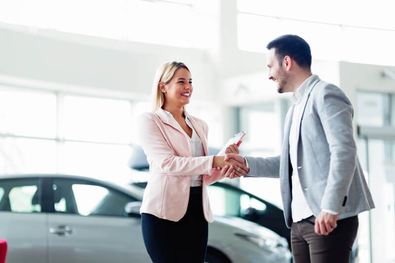 Two professionals shaking hands in a car showroom.