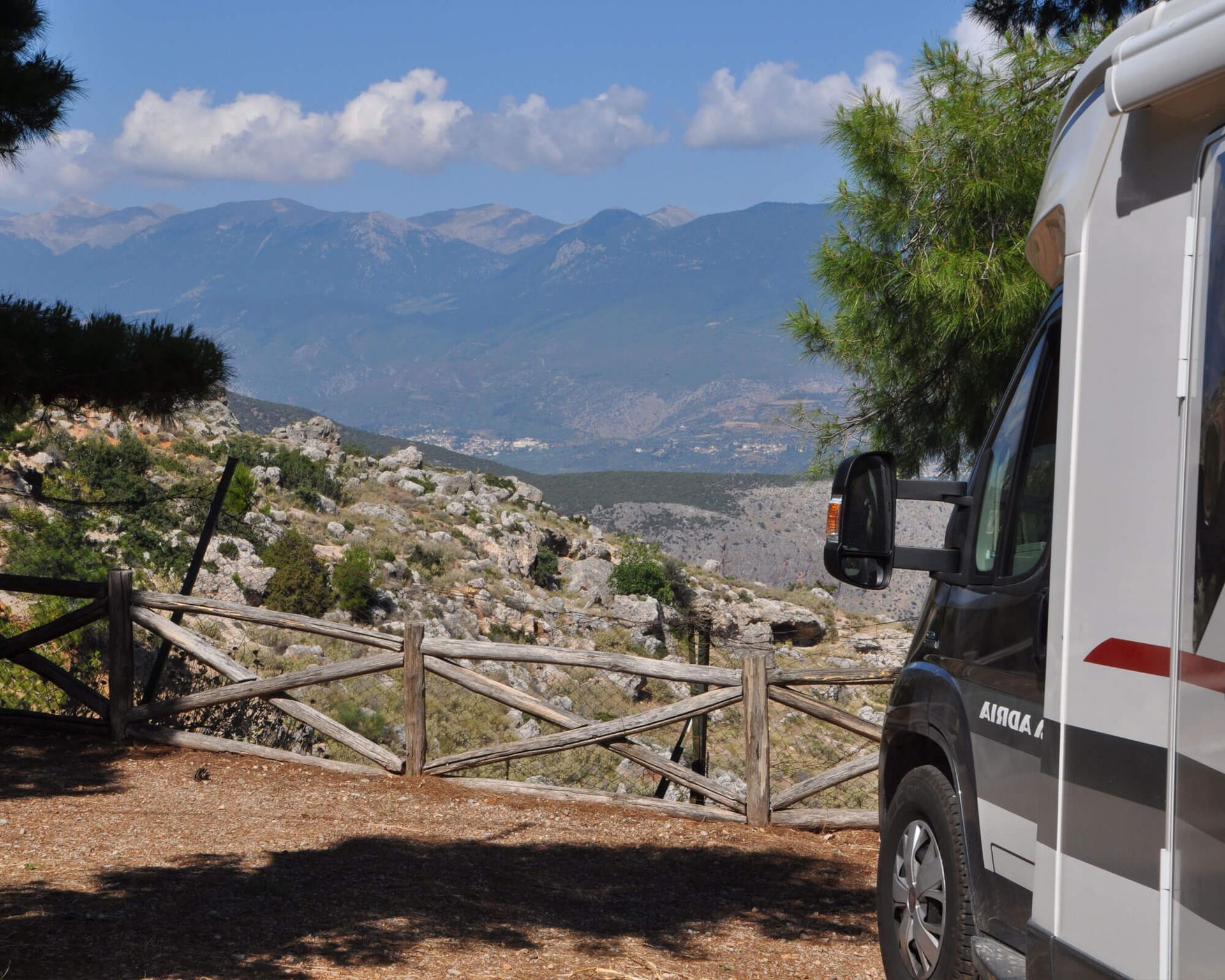 A motorhome parked by a wooden fence overlooking mountains and a blue sky.