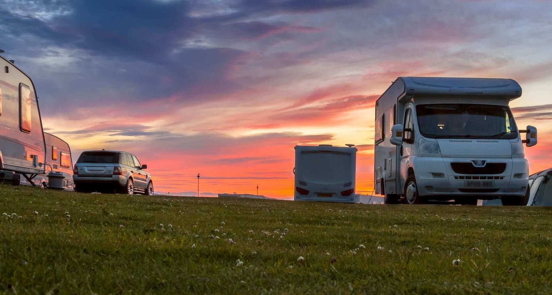 Caravan and motorhome parked on grass at dusk with vibrant sunset sky.