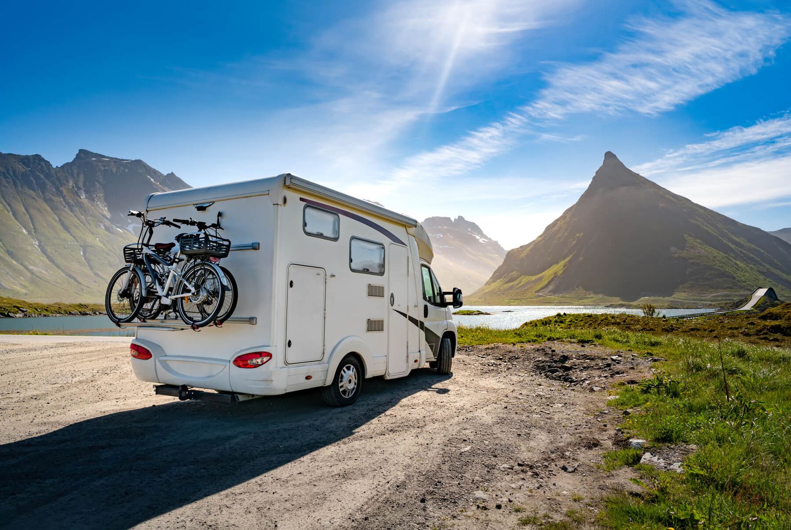 Motorhome with bikes parked by a lake with mountains in the backdrop.